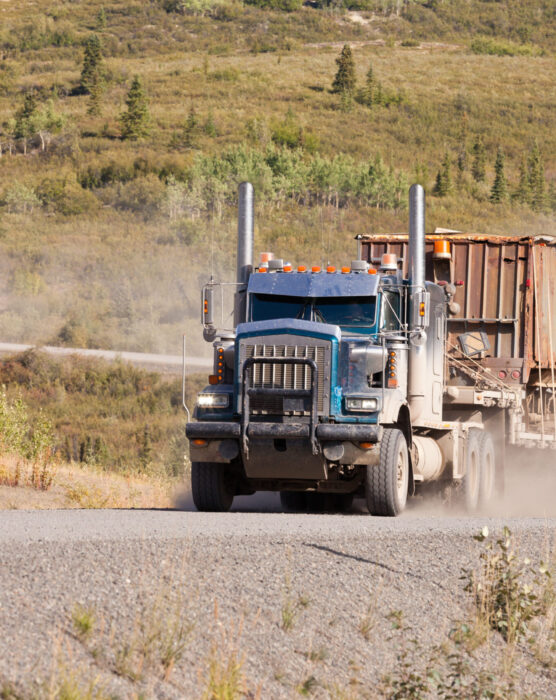 Heavy duty articulated industrial truck drives fast on remote gravel road throwing up dust
