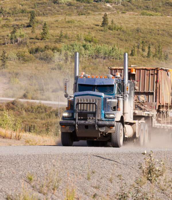 Heavy duty articulated industrial truck drives fast on remote gravel road throwing up dust