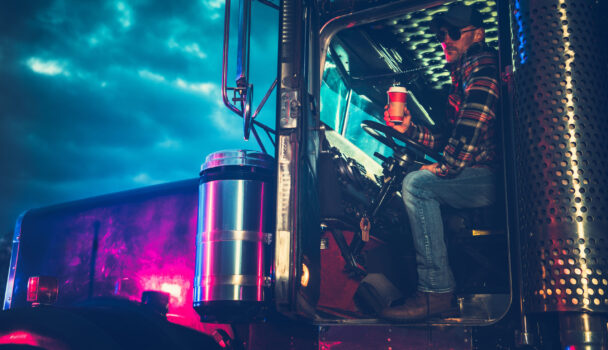 Trucker Driver Drinking a Coffee While on a Truck Stop. Heavy Duty Ground Transportation Theme.