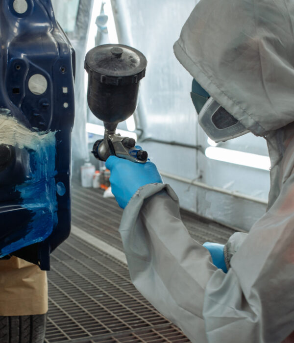 automobile repairman painter hand in protective glove with airbrush pulverizer painting car body in paint chamber