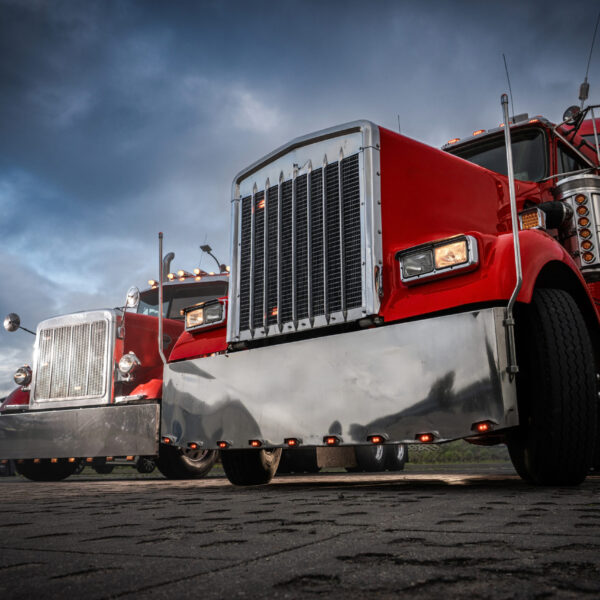 Two striking red trucks with shiny chrome accents are parked side by side against a dramatic twilight sky, capturing the essence of the trucking industry.