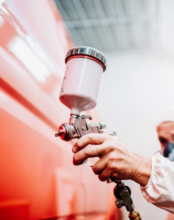 close up of worker painting a red car in a special garage, wearing a white costume