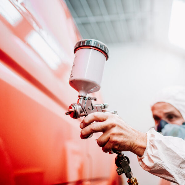 close up of worker painting a red car in a special garage, wearing a white costume