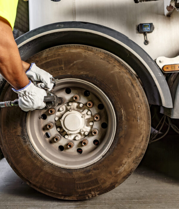 Side view of crop anonymous male mechanic in casual uniform and gloves using machine in tightening screw on wheel of truck while working in garage