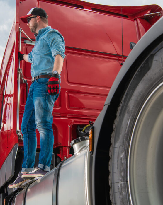Professional Caucasian Driver in His 30s Standing on a Semi Tractor Truck. Heavy Duty Transportation Industry.