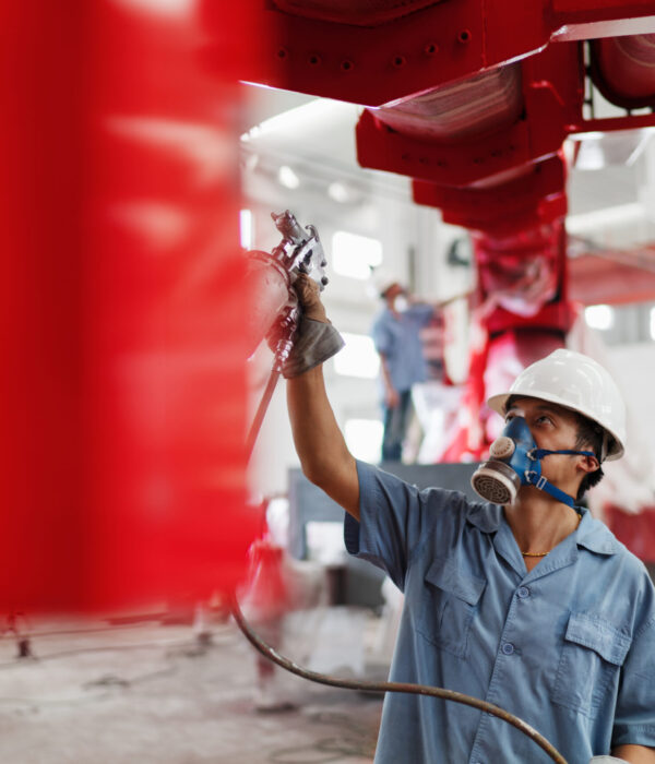 Male factory worker spray painting a red crane in factory workshop, China