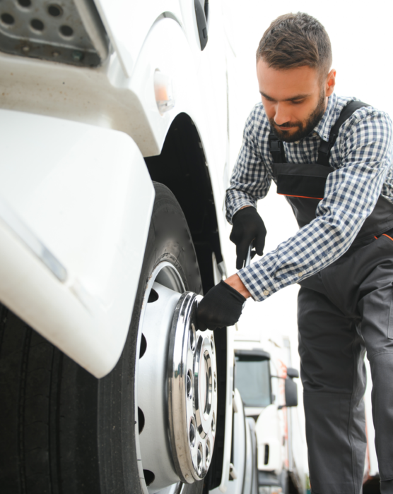 Working with damaged tire. Young truck driver is with his vehicle at daytime.
