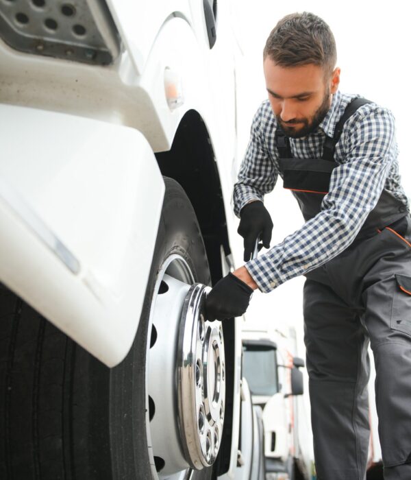 Working with damaged tire. Young truck driver is with his vehicle at daytime.