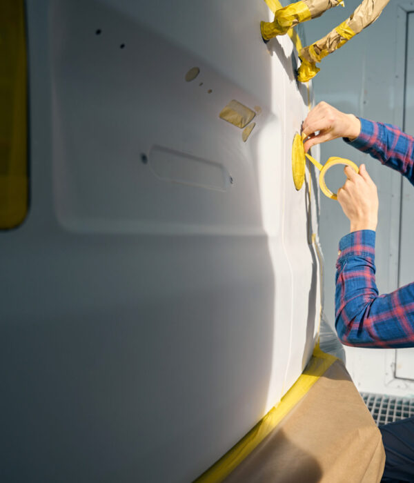 Professional man holds tape and seals parts on car. Surface preparation before painting automobile detail